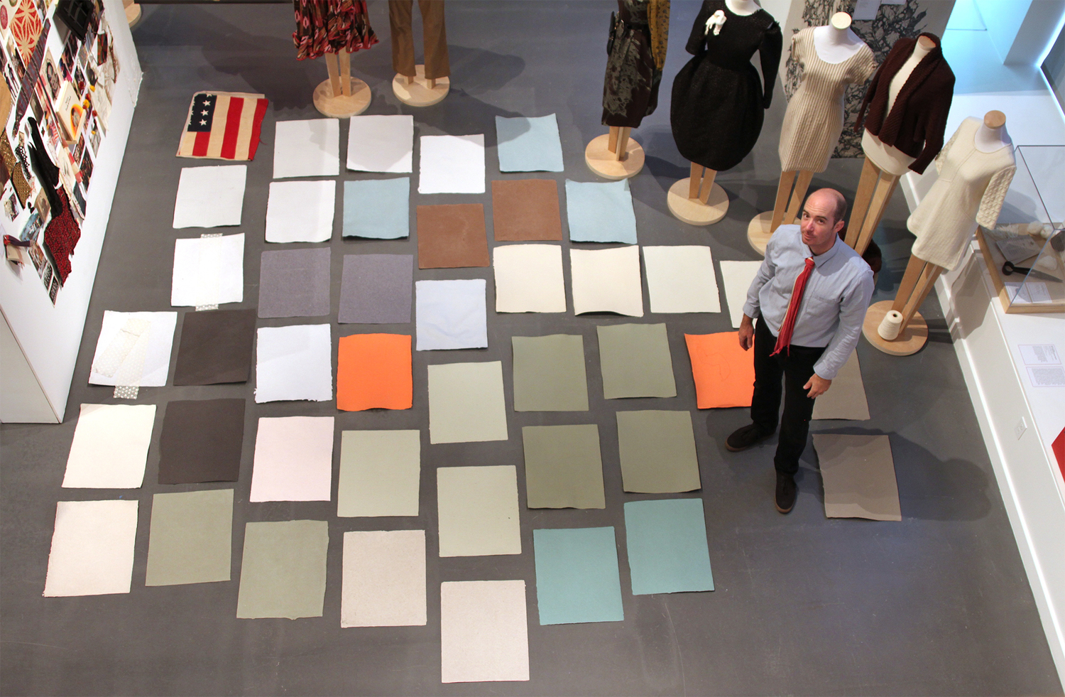 Drew Cameron stands stands beside many sheets of multi-colored paper arranged neatly on the floor
